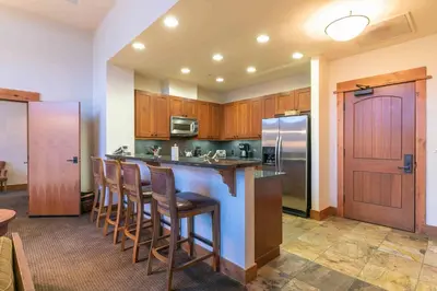 a kitchen with wooden cabinets and a bar with bar stools at Catamount Lodge 405B by East West Hospitality in Truckee