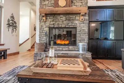 a living room with a stone fireplace and a chessboard at Leopard Lily Lodge Luxe Stays 2 Suites AC in Shaver Lake