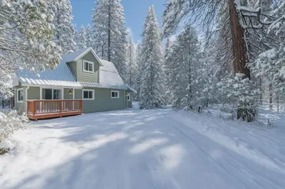 a green house in the snow with a driveway at The Sparrows Nest Cozy Charm Fire Pit Fun in Shaver Lake