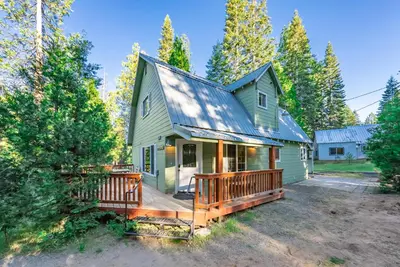 a green house with a porch and a deck at The Sparrows Nest Cozy Charm Fire Pit Fun in Shaver Lake