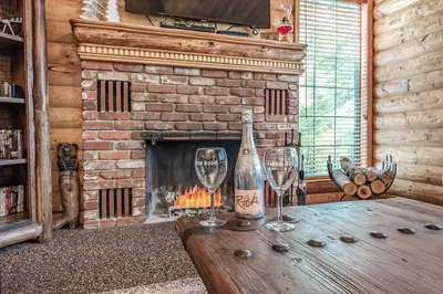 two wine glasses on a wooden table in front of a fireplace at The Stew Cabin Cozy Escape Fireside Memories in Shaver Lake