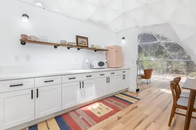 a kitchen with white cabinets and a large window at Dome Sweet Dome | Shaver Lake in Shaver Lake