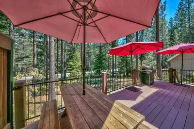 a deck with red umbrellas and a wooden table at Tahoe Townie - Cozy Cabin in South Lake Tahoe! in South Lake Tahoe