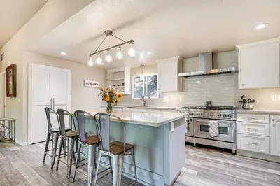a kitchen with white cabinets and a blue island with chairs at Mtn-View Gem Deck, Grill and Fire Pit in West Point in Volcano