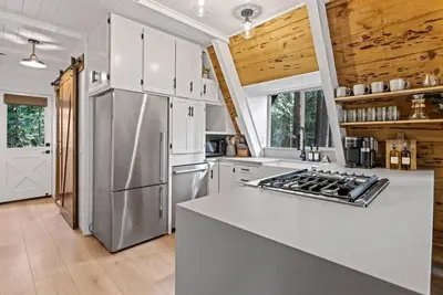 a kitchen with white cabinets and a stainless steel refrigerator at The Sugar Pine Speakeasy in Homewood