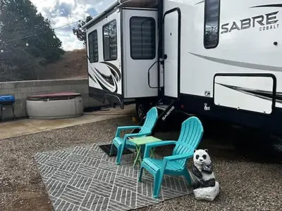 a dog sitting next to two chairs and an rv at Puffy Panda RV-Hot Tub-Sleeps 2 in Ahwahnee