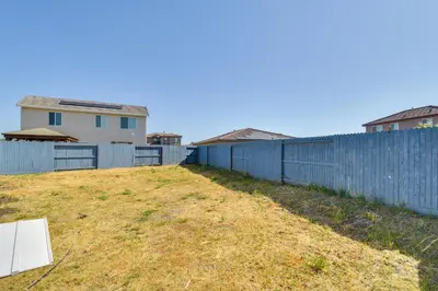 a fence and a yard with a house behind it at WFH-Friendly Getaway with Yard in Manteca! in Manteca