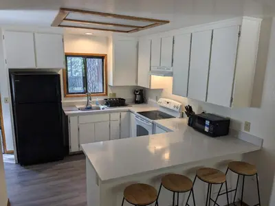 a kitchen with white cabinets and a black refrigerator and stools at Bulldog Den in Twain Harte