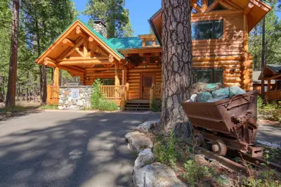 a log cabin with a wheelbarrow in front of a tree at Yosemite's Luxury Estate in North Wawona