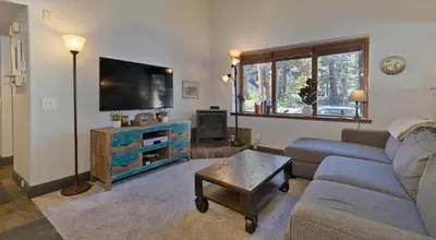 a living room with a couch and a flat screen tv at Ski Den - Steps to Mammoth Village! in Mammoth Lakes