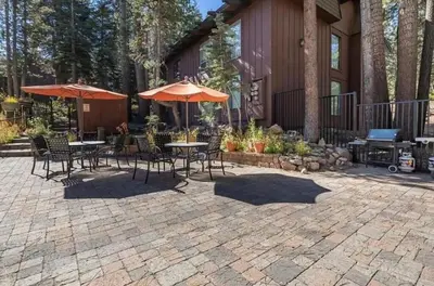 a patio with tables and chairs and umbrellas at Ski Den - Steps to Mammoth Village! in Mammoth Lakes