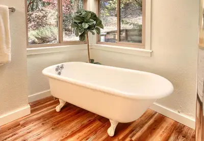 a white bath tub in a bathroom with two windows at Tranquility House-Riverfront-Fireplace-Sleeps six in Oakhurst