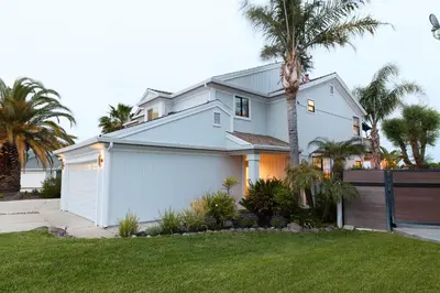 a white house with a fence and palm trees at Marlin Cove Pet Friendly Waterfront Retreat in Discovery Bay