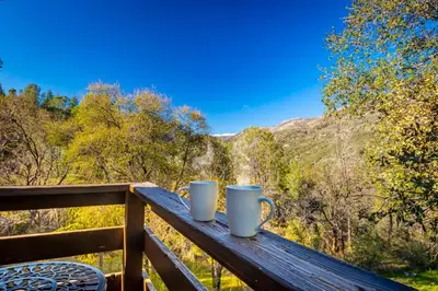 two coffee mugs sitting on a wooden rail on a balcony at Sierra Vista Lookout Lodge for 8 people with Hot tub, deck and trail to waterfalls in North Fork