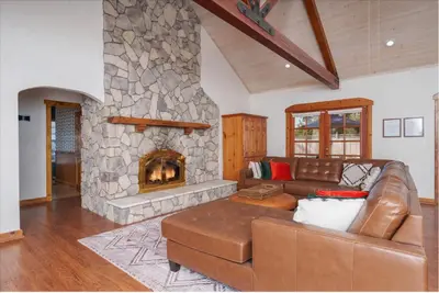 a living room with a couch and a stone fireplace at Cedar Creek Lodge with POOL/hot tub/sleeps 24 in Oakhurst