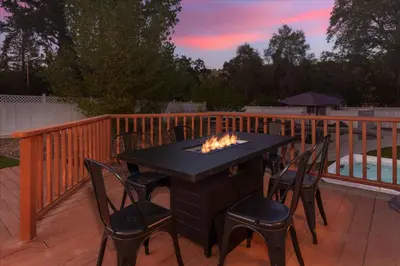 a black table and chairs on a deck with a fireplace at Cedar Creek Lodge with POOL/hot tub/sleeps 24 in Oakhurst