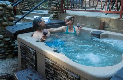 a man and woman in a hot tub with a glass of wine at Cozy Yosemite Cabin with Hot Tub in the Pines in Fish Camp