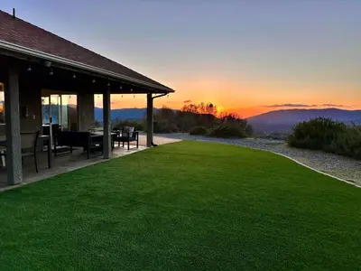 a house with a green lawn with the sunset in the background at Yosemite Vista Highlands in Oakhurst