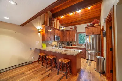 a kitchen with wooden cabinets and a kitchen island with bar stools at Plush Mammoth Condo w Balcony Views in Mammoth Lakes