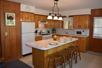 a kitchen with wooden cabinets and a island with bar stools at Sequoia House at The Redwoods in Wawona