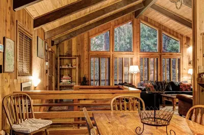 a living room with a table and some windows at Tyler's Timber Lodge in Wawona