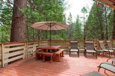 a wooden deck with a table and chairs and an umbrella at Pohono Pines in Wawona