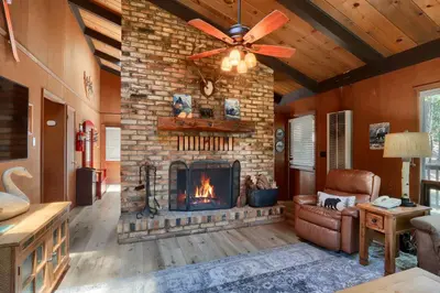 a living room with a fireplace and a ceiling fan at Hiltbrand Hangout in Wawona