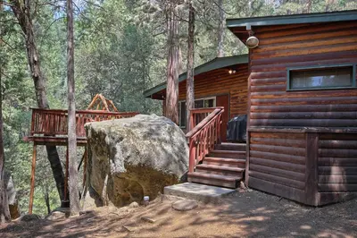 a log cabin with a staircase and a large rock at The Tree House in Wawona