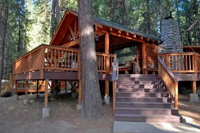 a log cabin in the woods with stairs and a tree at Deer Den in Wawona