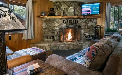 a living room with a stone fireplace and couches at Pine Creek Cabin in Wawona