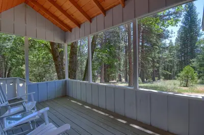a screened porch with two rocking chairs and trees at Edna's Hearts Desire in Wawona