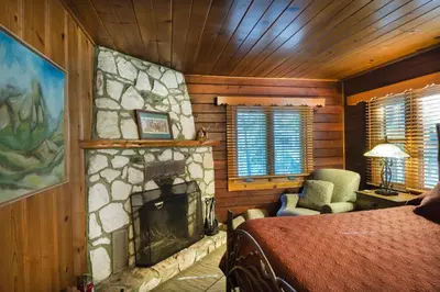 a bedroom with a stone fireplace with a bed and a chair at Sugar Pine Suite in Wawona