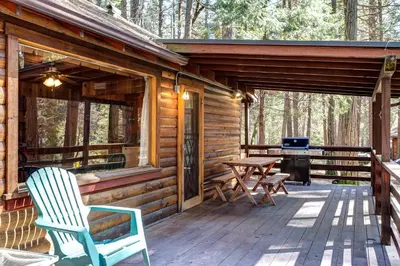 a cabin with a deck with a grill and chairs at Mia Mora in Wawona