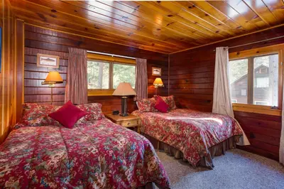 two beds in a room with wooden walls and windows at Hansen Cabin in Wawona