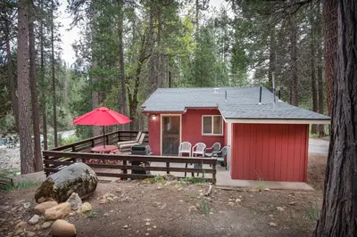 a red cabin in the woods with a table and chairs at Sparrow's Nest in Wawona