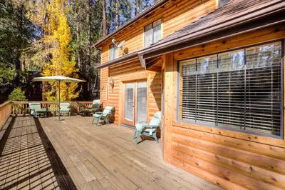 a cabin with a wooden deck with a table and chairs at Cedar Lodge in Wawona