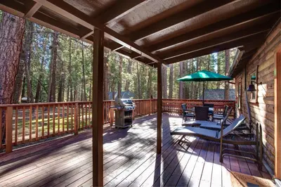 a deck with a grill and a chair and umbrella at Our Yosemite Getaway in Wawona