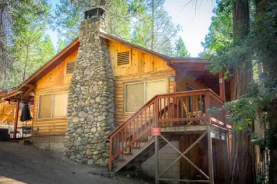 a cabin in the woods with a stone chimney and a staircase at Howard's Retreat in Wawona