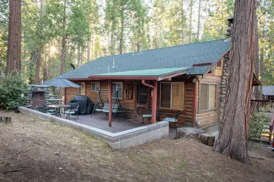 a log cabin with a deck in the woods at Howard's Retreat in Wawona