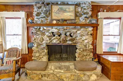 a stone fireplace in a living room with a table at Chatterton's Cottage in Wawona