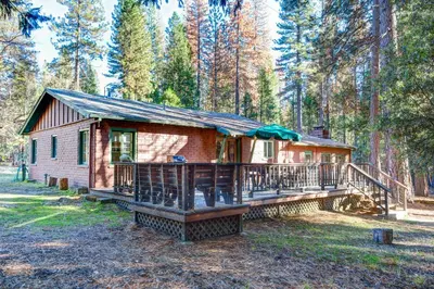 a cabin in the woods with a large deck at Ashbaugh Meadow in Wawona