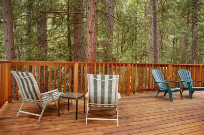 three chairs and a table on a deck with trees at Harmony Villa in Wawona