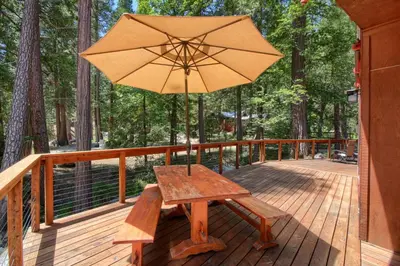a wooden bench with an umbrella on a deck at Jolie Cabin in Wawona