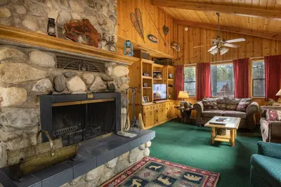 a living room with a fireplace and a stone wall at Deer Lodge in Wawona