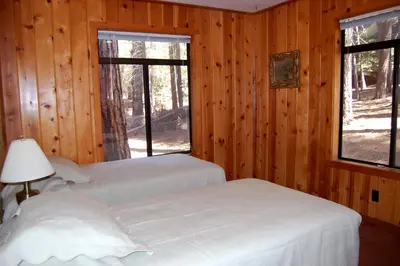 two beds in a room with wooden walls and windows at Burke's Place in Wawona