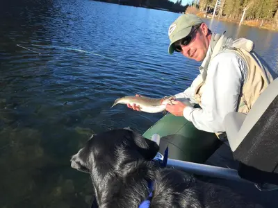 a man holding a fish in a boat with a dog at Mountainback 19 Loft Den in Mammoth Lakes