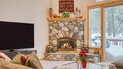 a living room with a stone fireplace with a tv at Pinewood Lodge by AvantStay Cozy Cabin Near Ski Resorts Hiking in Truckee