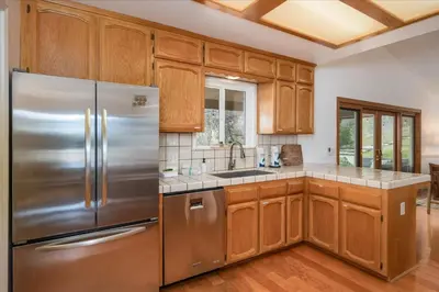 a kitchen with wooden cabinets and stainless steel refrigerator at New Big Sky Cabin at Yosemite w/ VIEWS, hot tub, firepit, and more in Oakhurst