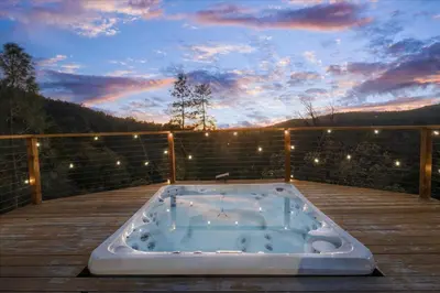 a jacuzzi tub on a deck with a sunset at New Yosemite Dream Nest with HUGE views/spa/firepit/pet friendly in Oakhurst