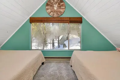 a room with two beds and a window with a clock at CC Cabin - Full Game Room & Wrap Around Deck in Shaver Lake